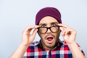 Young guy holding eyeglasses with shocked expression